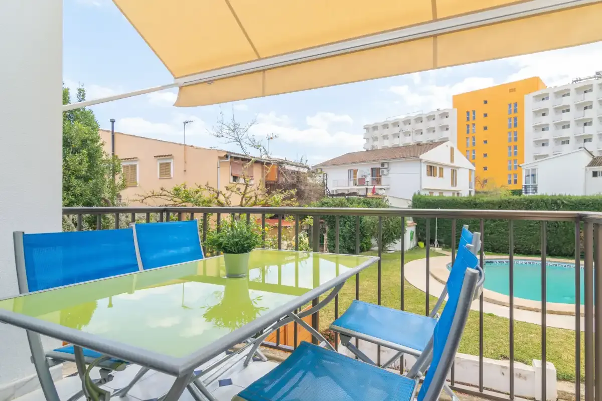 A balcony seating area overlooks a swimming pool and nearby buildings.