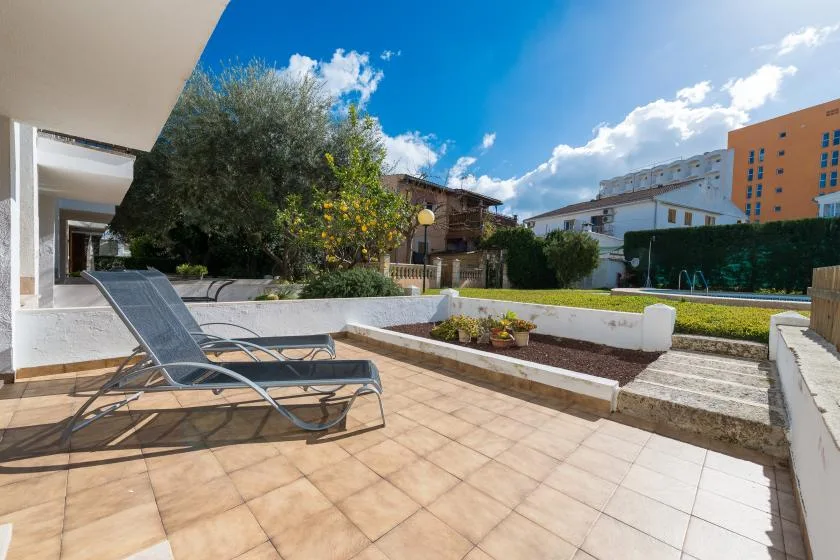 A sunny outdoor terrace has lounge seating beside planted garden beds.
