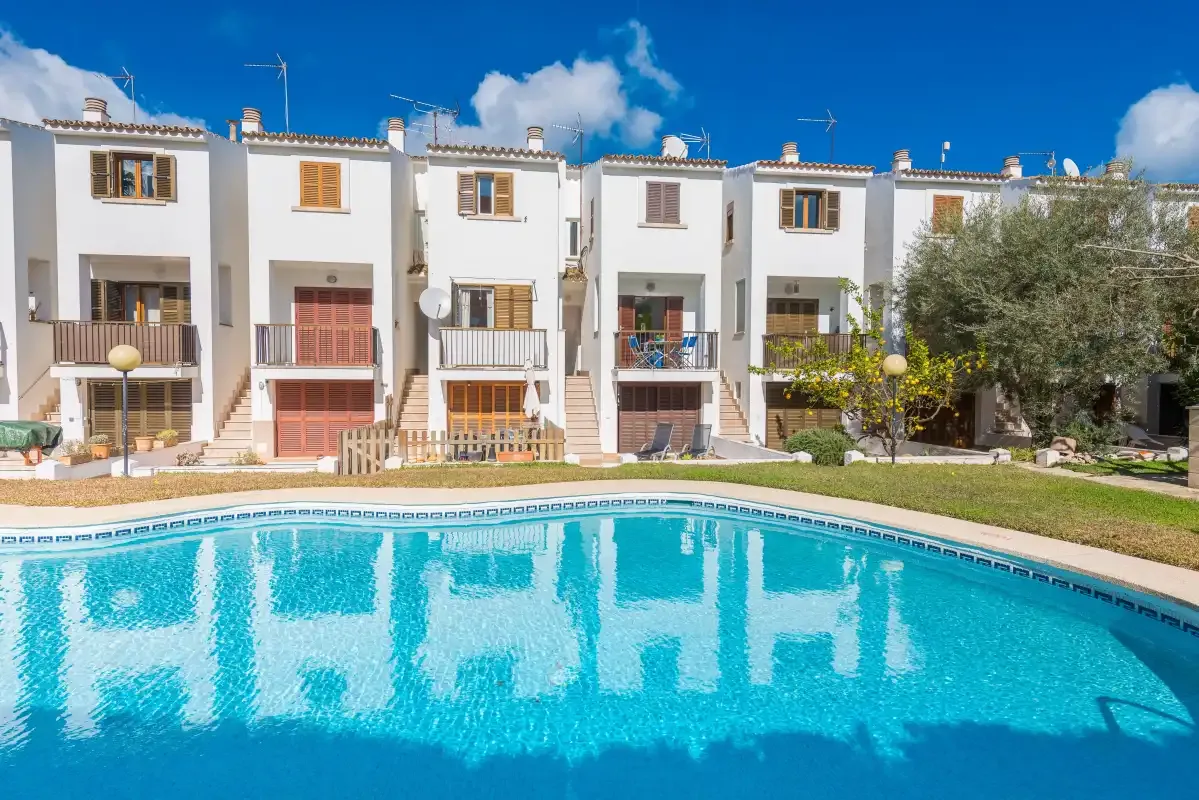 A row of white homes stands beside a curved swimming pool.