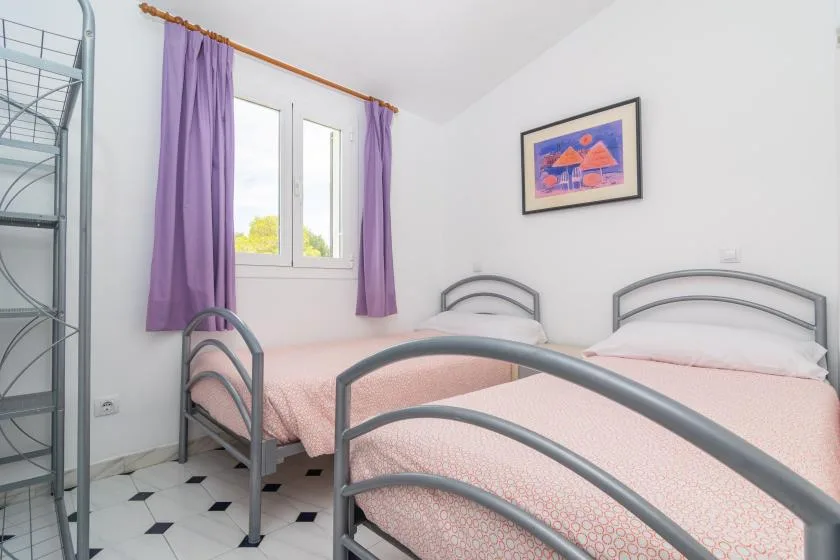 A bedroom with two beds, a window, and purple curtains.