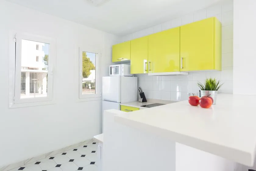A bright kitchen with yellow cabinets, white counters, and windows.
