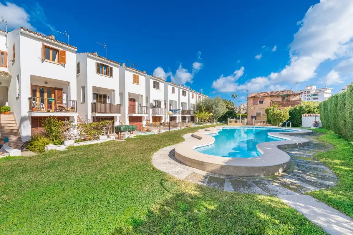A swimming pool and grassy courtyard sit in front of a row of white buildings.