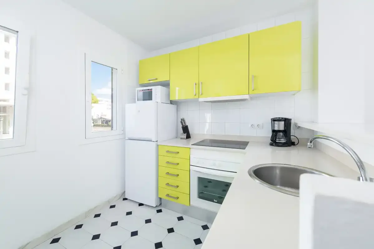 A bright kitchen with yellow cabinets, a refrigerator, and a sink.