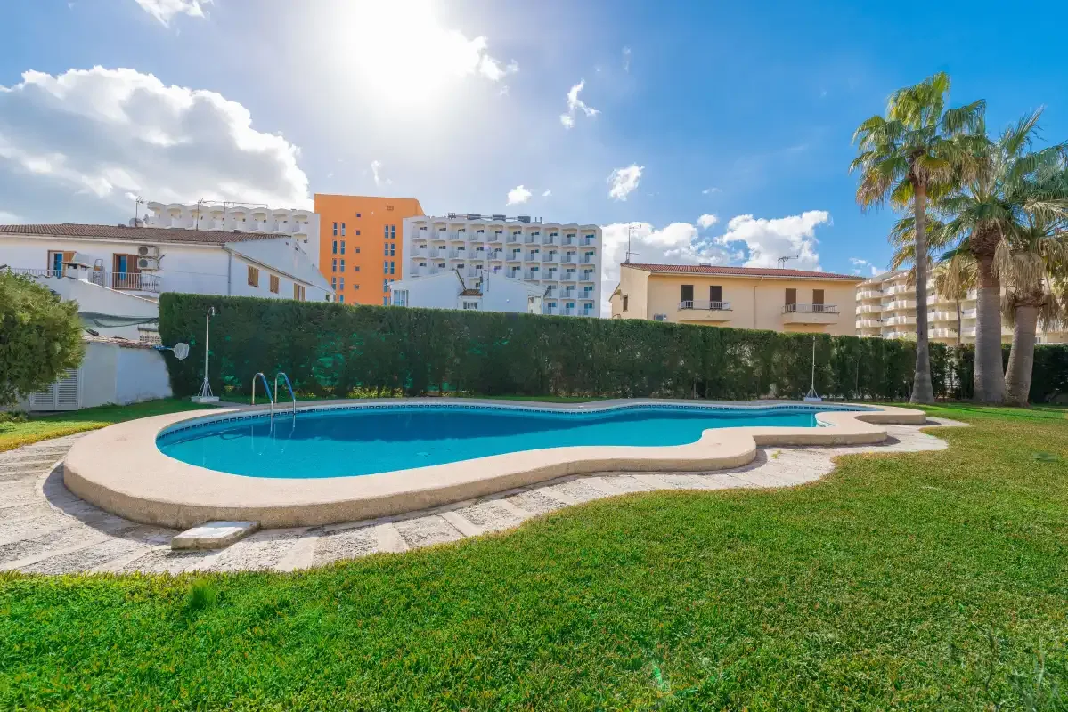 An outdoor swimming pool sits in a grassy courtyard surrounded by buildings.