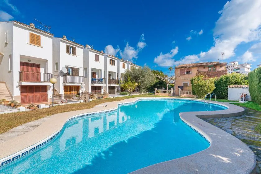 A bright outdoor swimming pool sits in front of a row of white residential buildings.