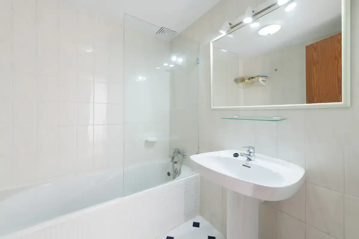 A tiled bathroom with a bathtub, sink, and wall mirror.
