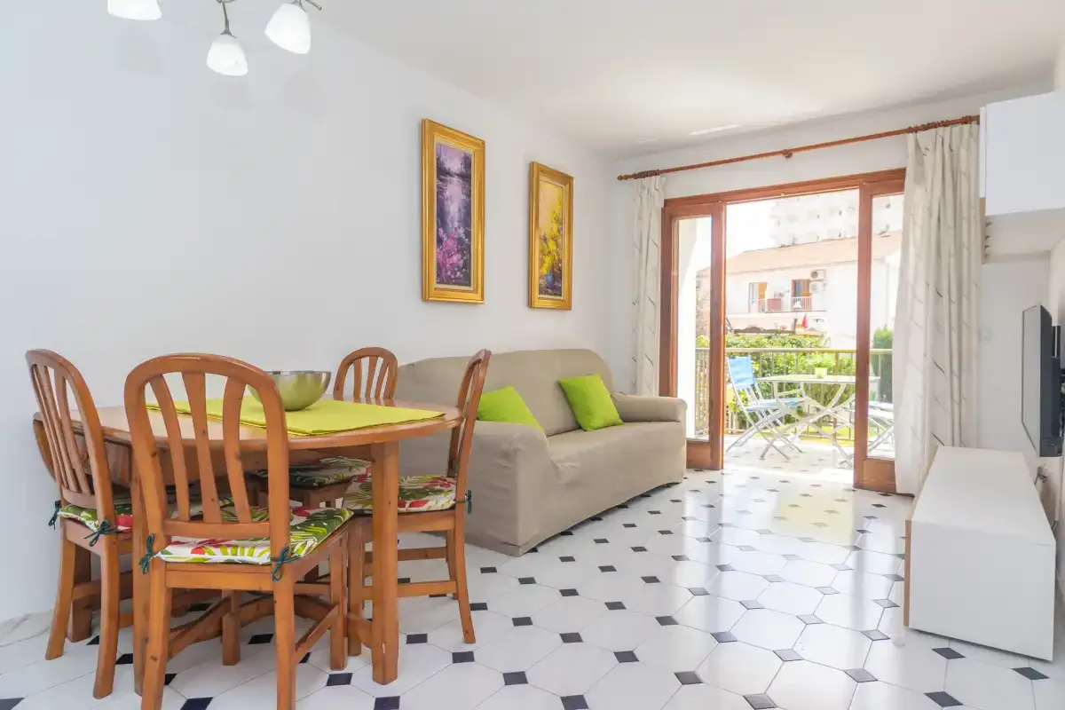 Living and dining area with a wooden dining table beside a sofa and balcony doors.