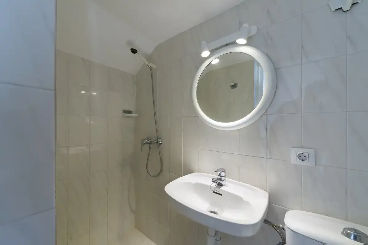 A tiled bathroom with a sink, illuminated mirror, and shower.