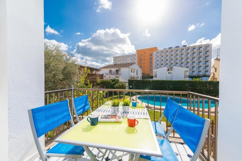 A balcony dining area overlooks a swimming pool and nearby buildings.
