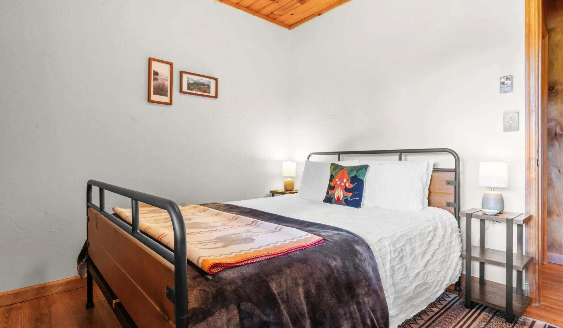 Un dormitorio con una cama de estructura metálica, ropa de cama colorida y mesitas de noche.