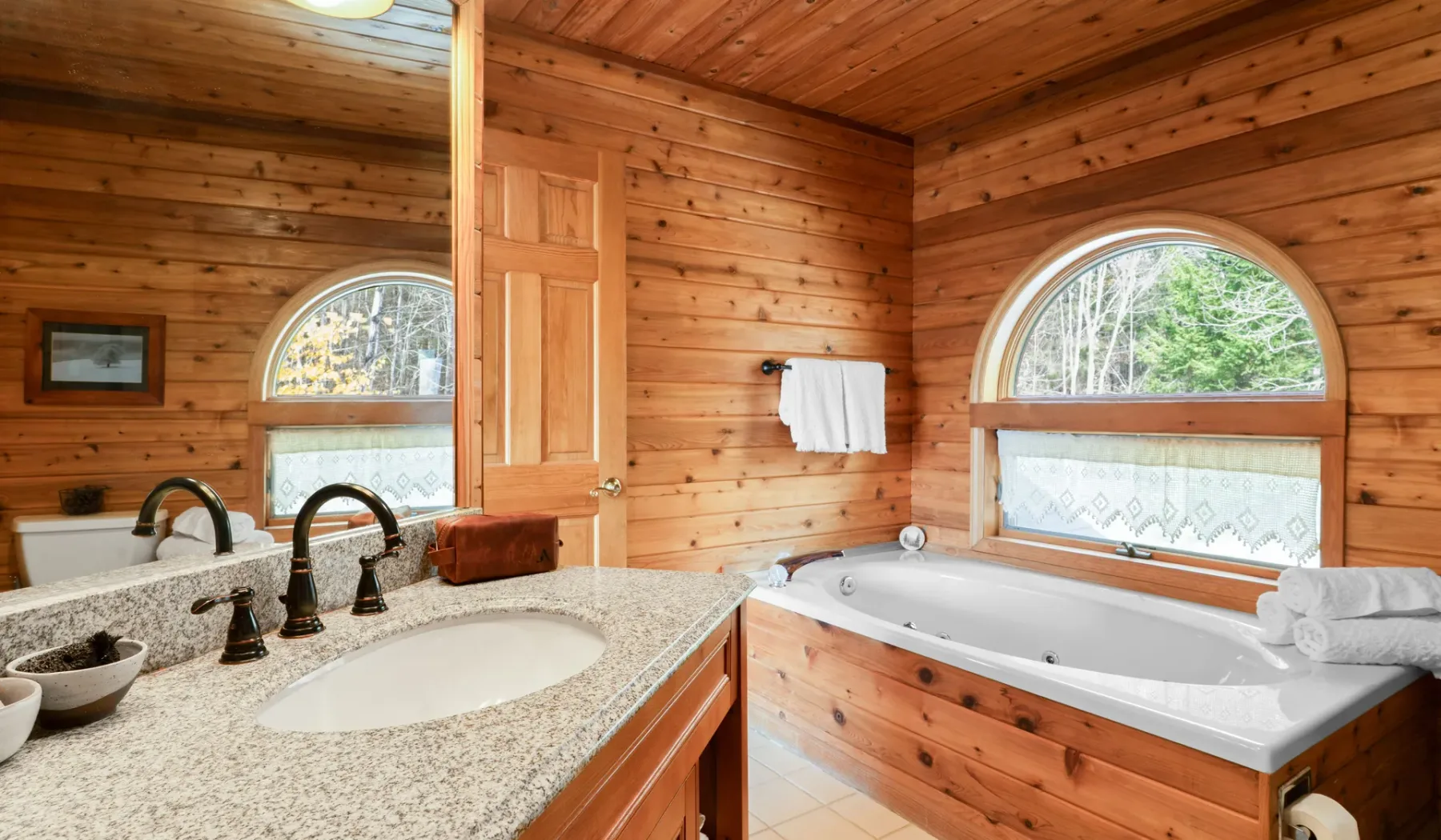 Un baño revestido de madera con lavabo y bañera bajo una ventana arqueada.