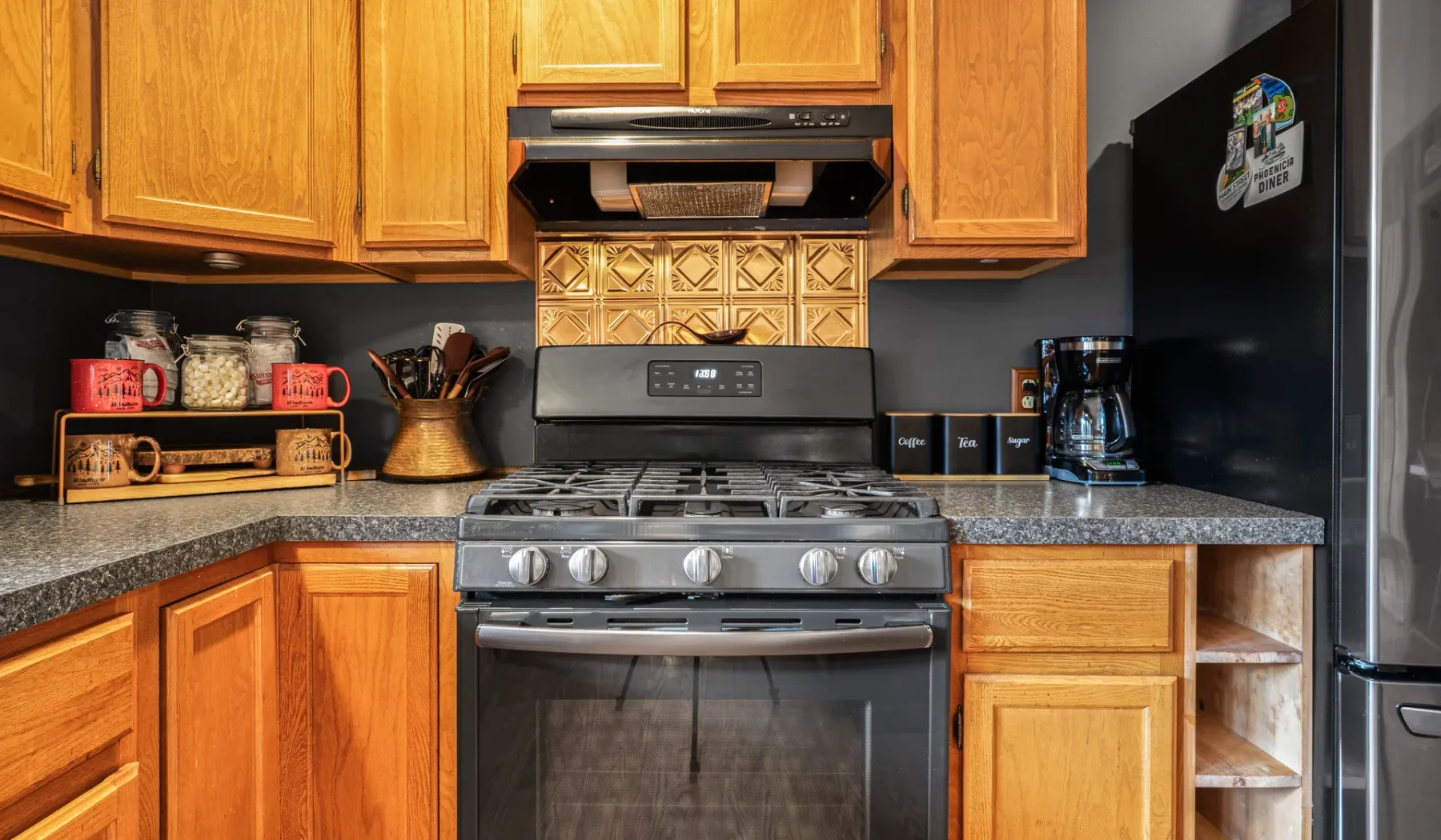 Una cocina con gabinetes de madera, una estufa y encimeras oscuras.