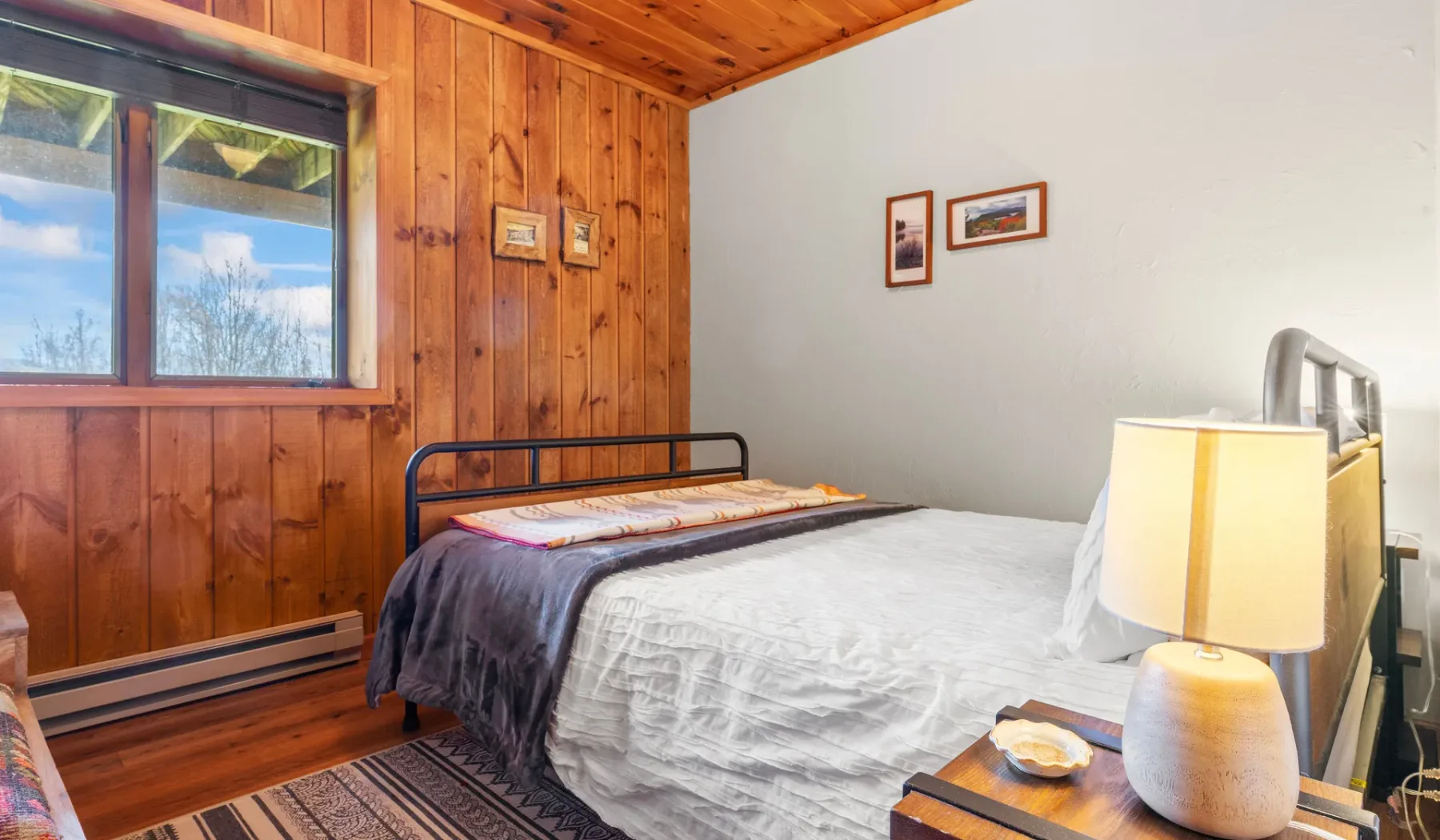 Un dormitorio con una cama junto a una pared revestida de madera y una ventana.