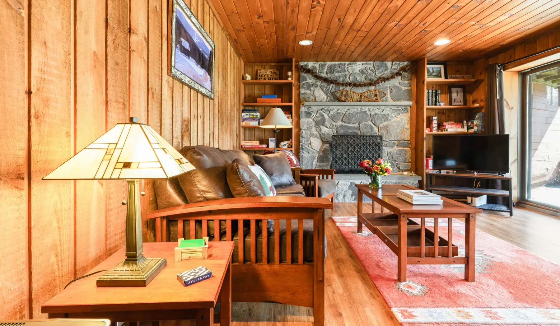 Una sala de estar revestida de madera con asientos, chimenea de piedra y televisor.
