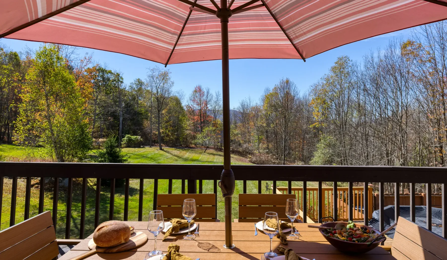 Una zona de comedor al aire libre bajo una sombrilla a rayas da a un paisaje arbolado.