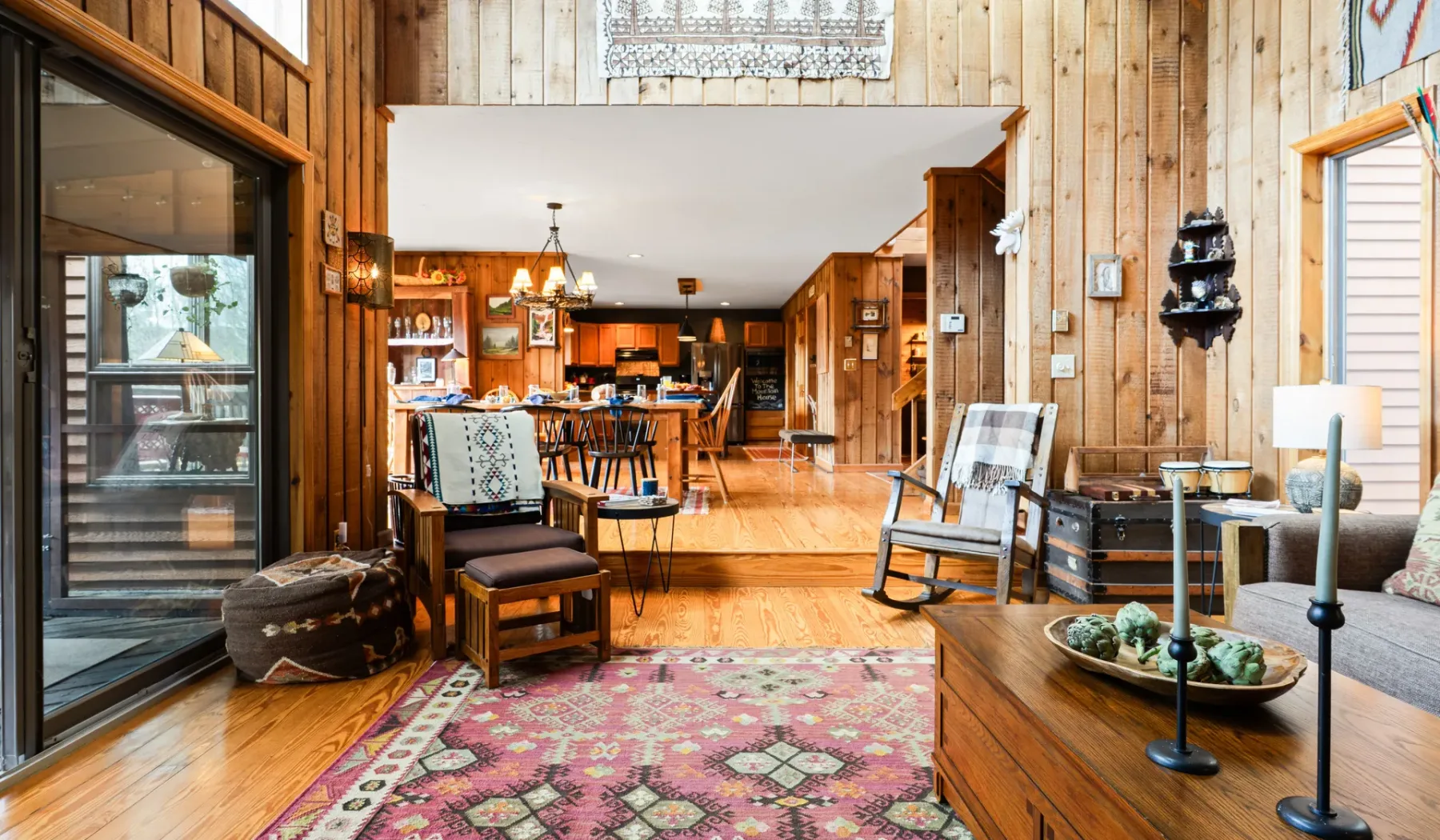 Una sala con paneles de madera se abre a un comedor, con asientos y una alfombra estampada.