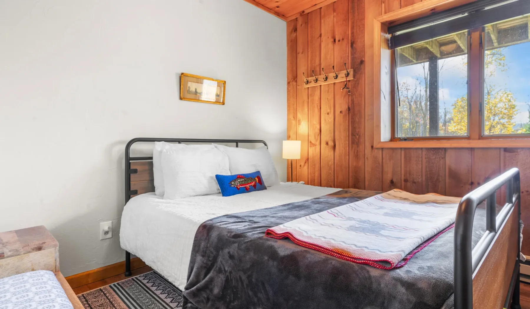 Un dormitorio con una cama junto a una pared revestida de madera y una ventana grande.