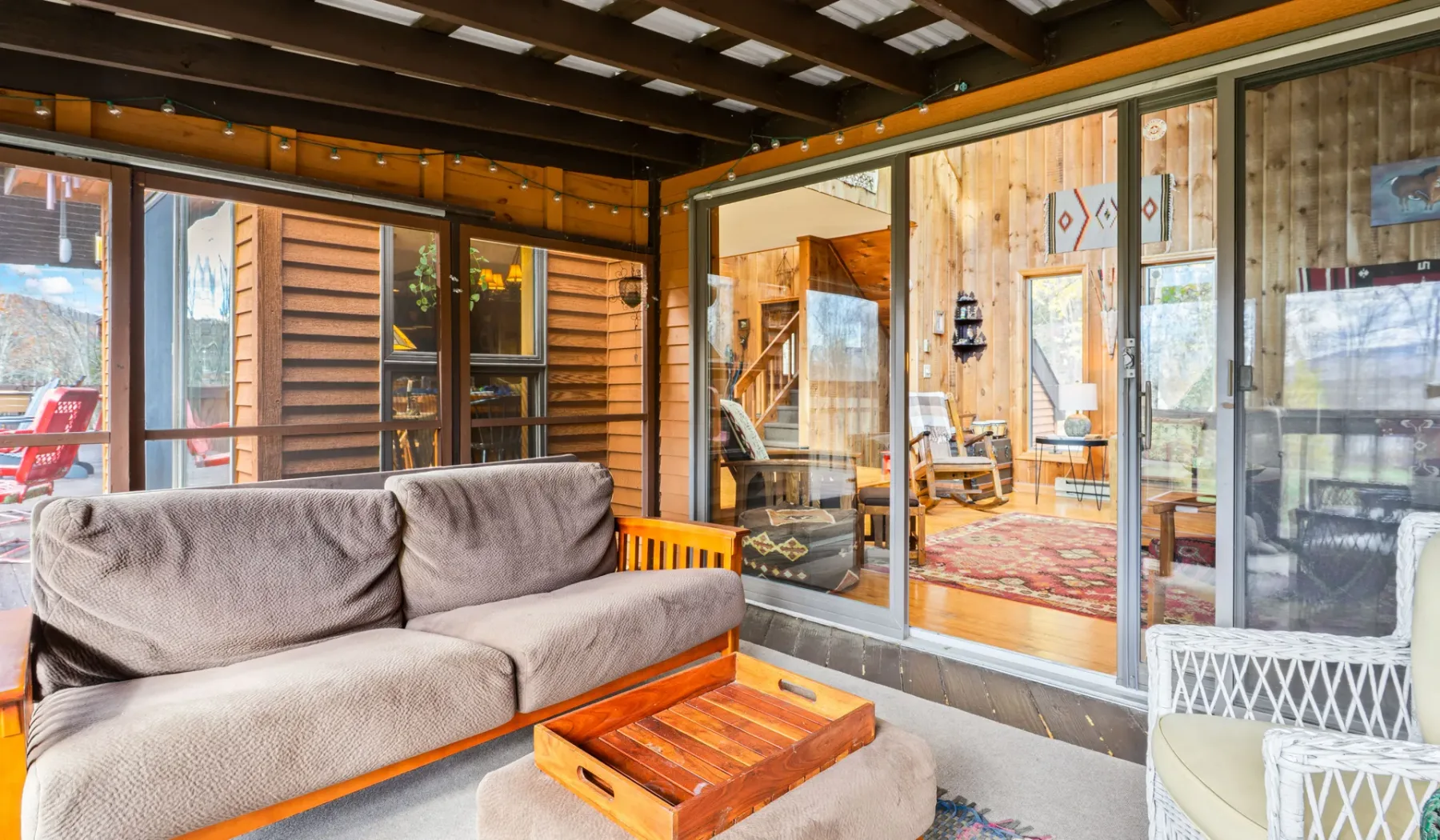 Un patio cubierto con asientos acolchados y grandes puertas de vidrio que dan a una habitación revestida de madera.