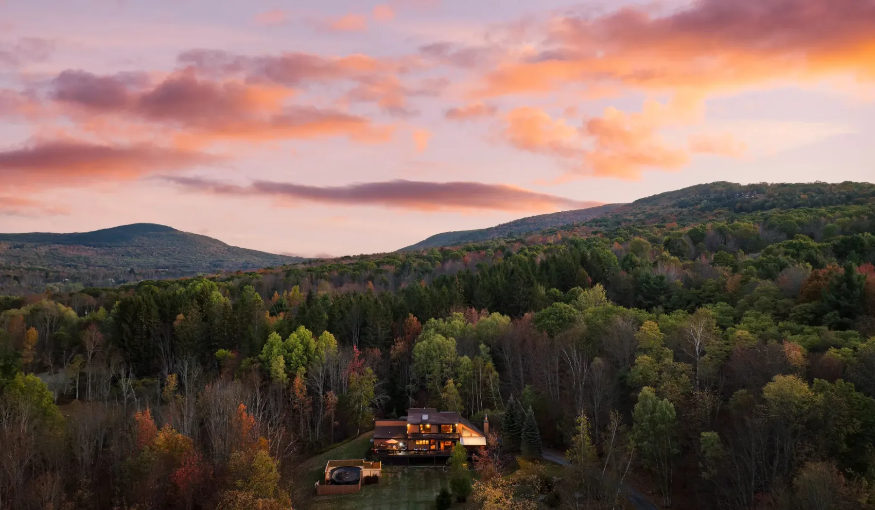 Un paisaje de montaña cubierto de bosques rodea un pequeño edificio bajo un cielo colorido al atardecer.