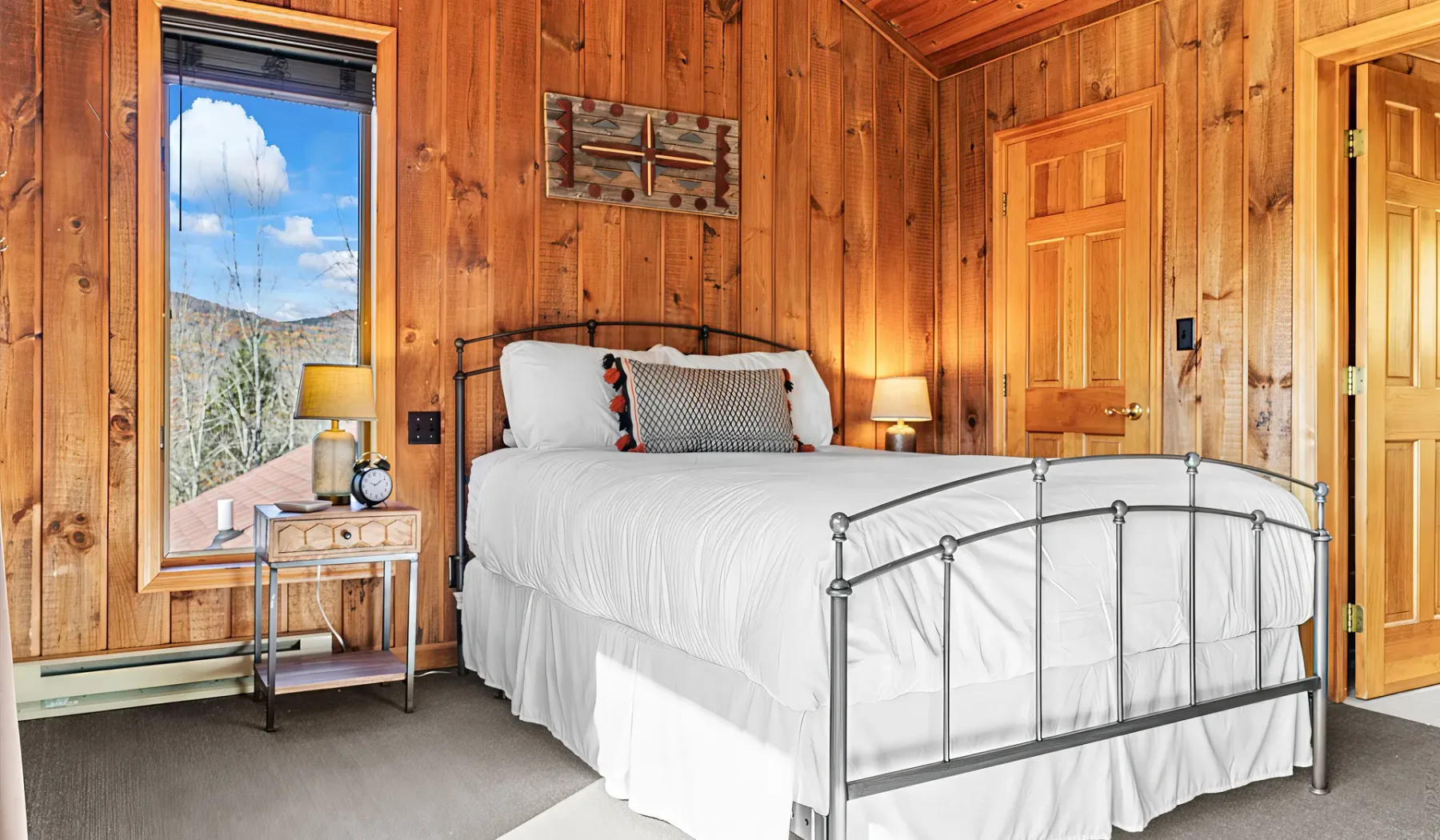 Un dormitorio con una cama blanca, paredes de madera y una ventana con vista a los árboles.