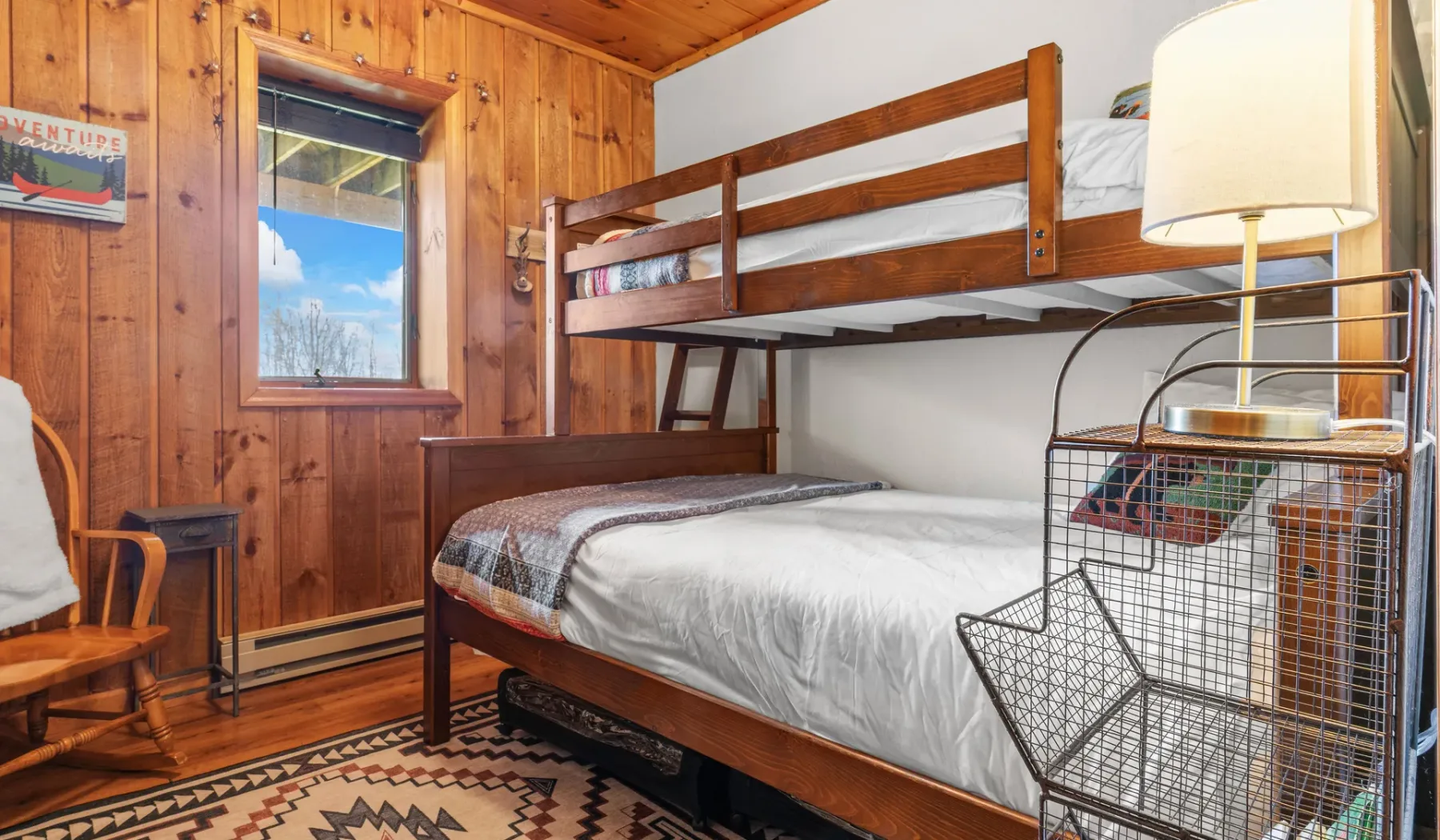 Un dormitorio con paredes de madera, literas, una ventana y una alfombra estampada.