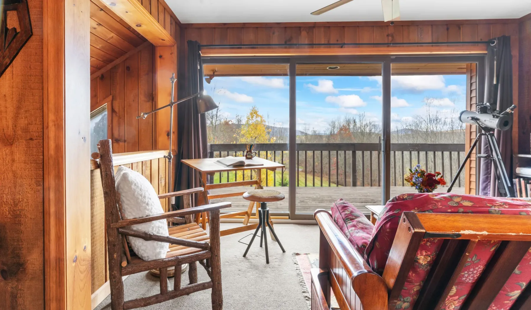 Una sala revestida de madera da a un balcón con vistas arboladas.