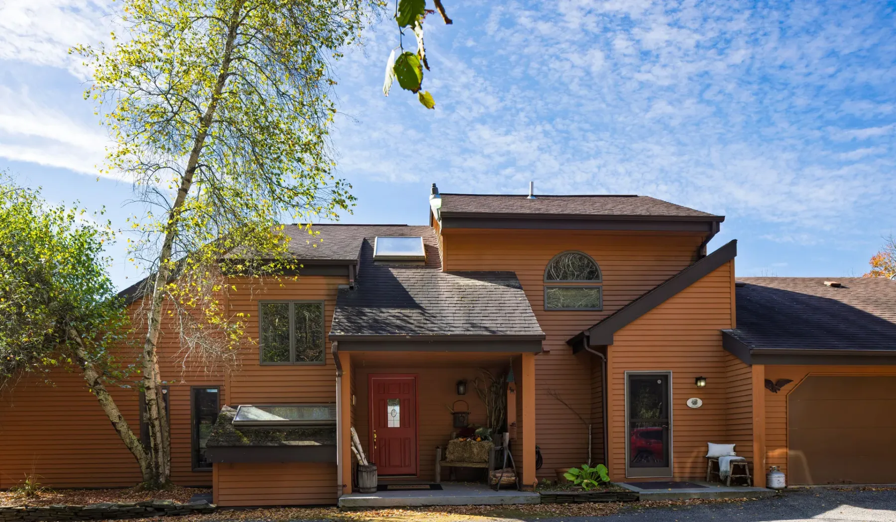 Una casa revestida de madera, con una puerta roja y árboles frondosos cerca.