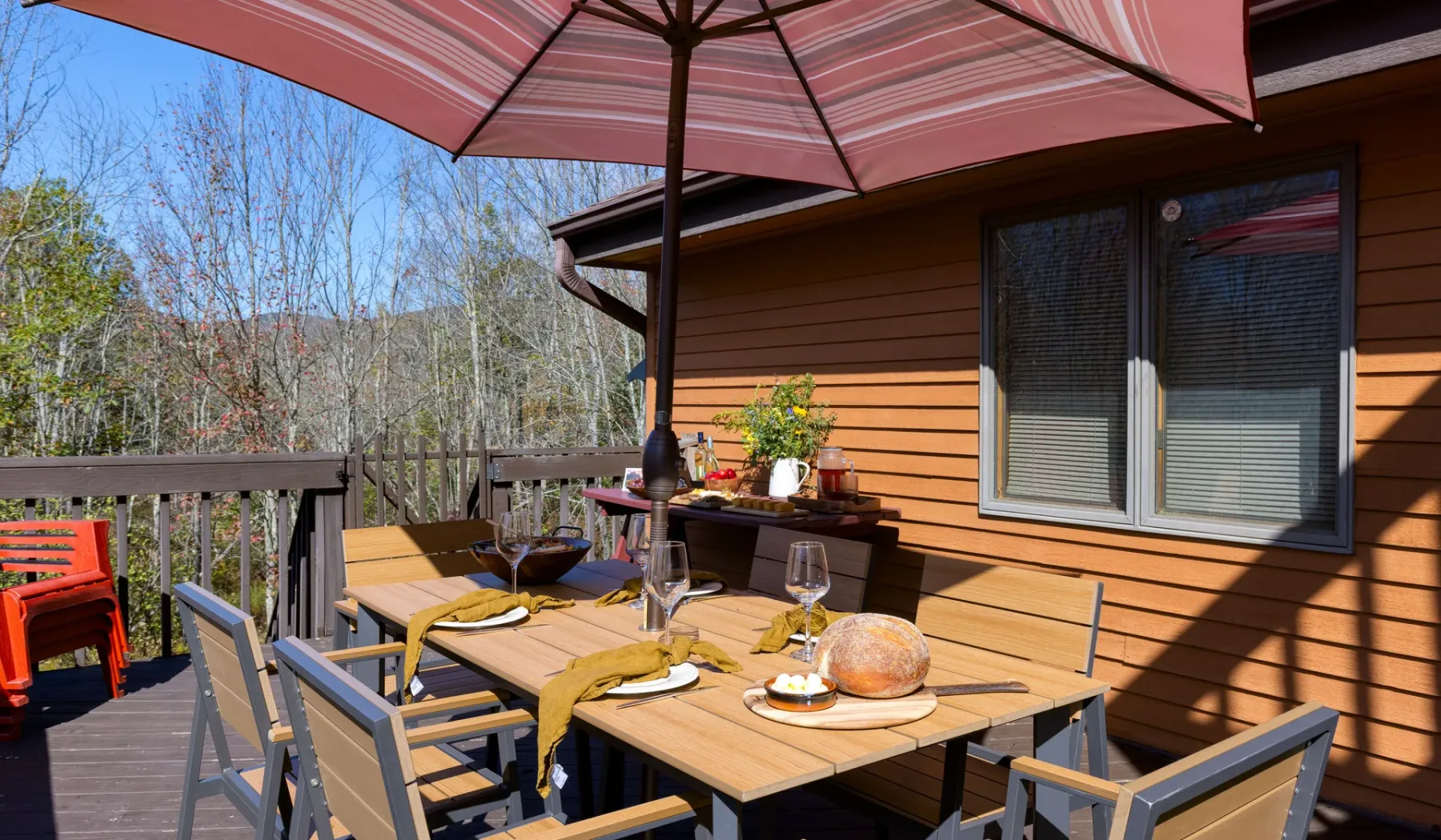 Un comedor al aire libre está en una terraza de madera junto a una casa de revestimiento marrón.