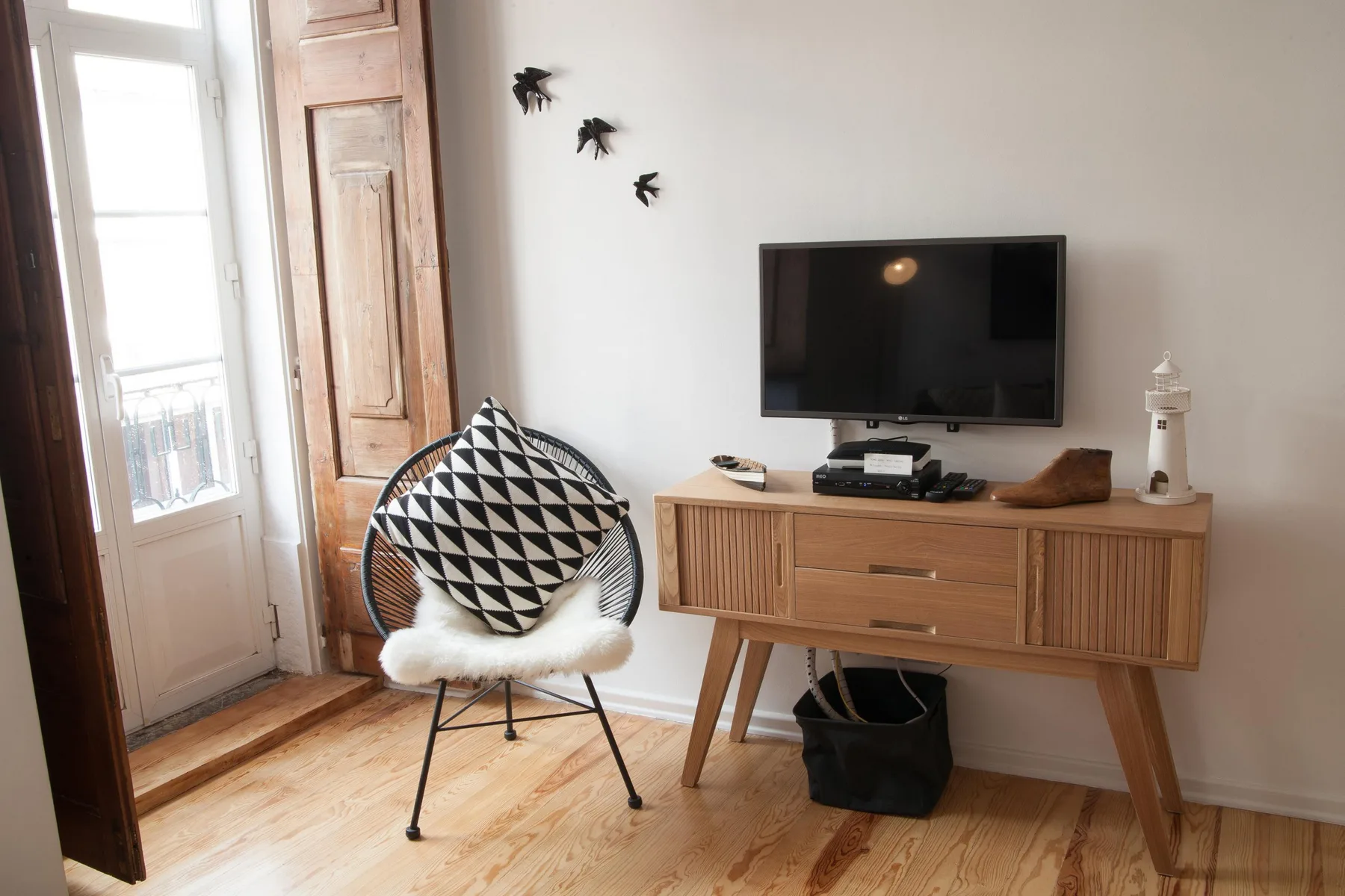 A living room with a television, wooden cabinet, and patterned seating by the window.
