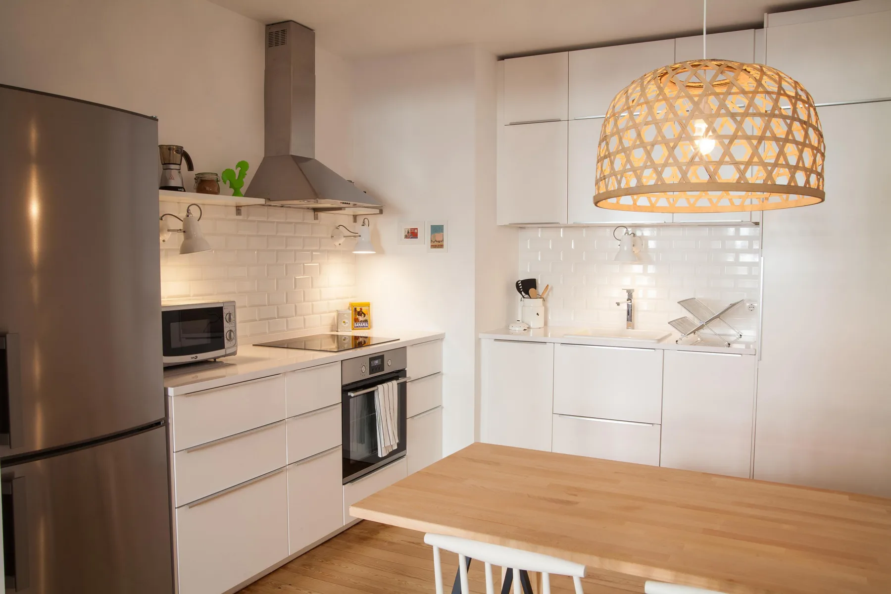 A bright kitchen with white cabinetry, stainless steel appliances, and a wooden dining table.