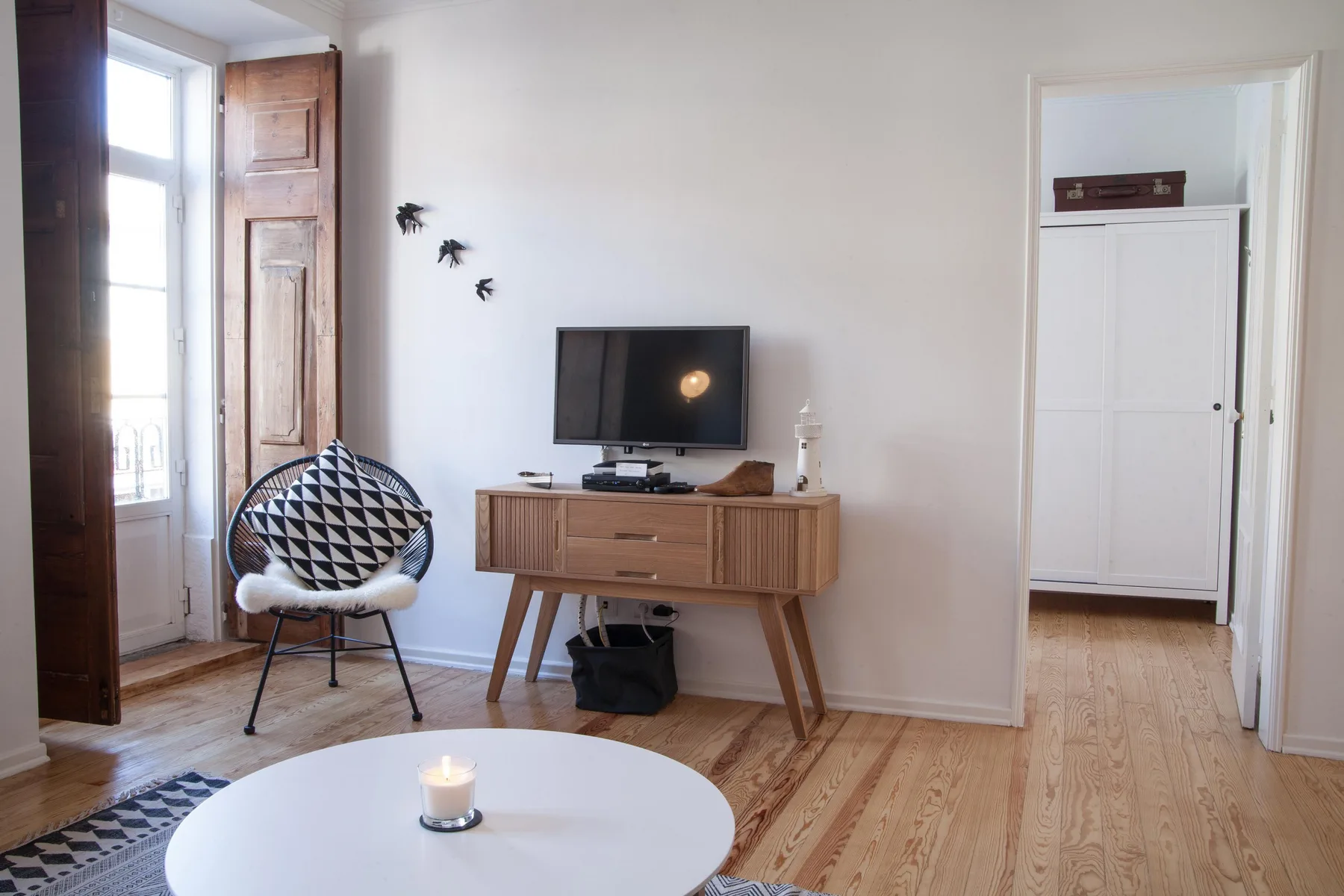 A bright living room with a television, wooden cabinet, and patterned seating.