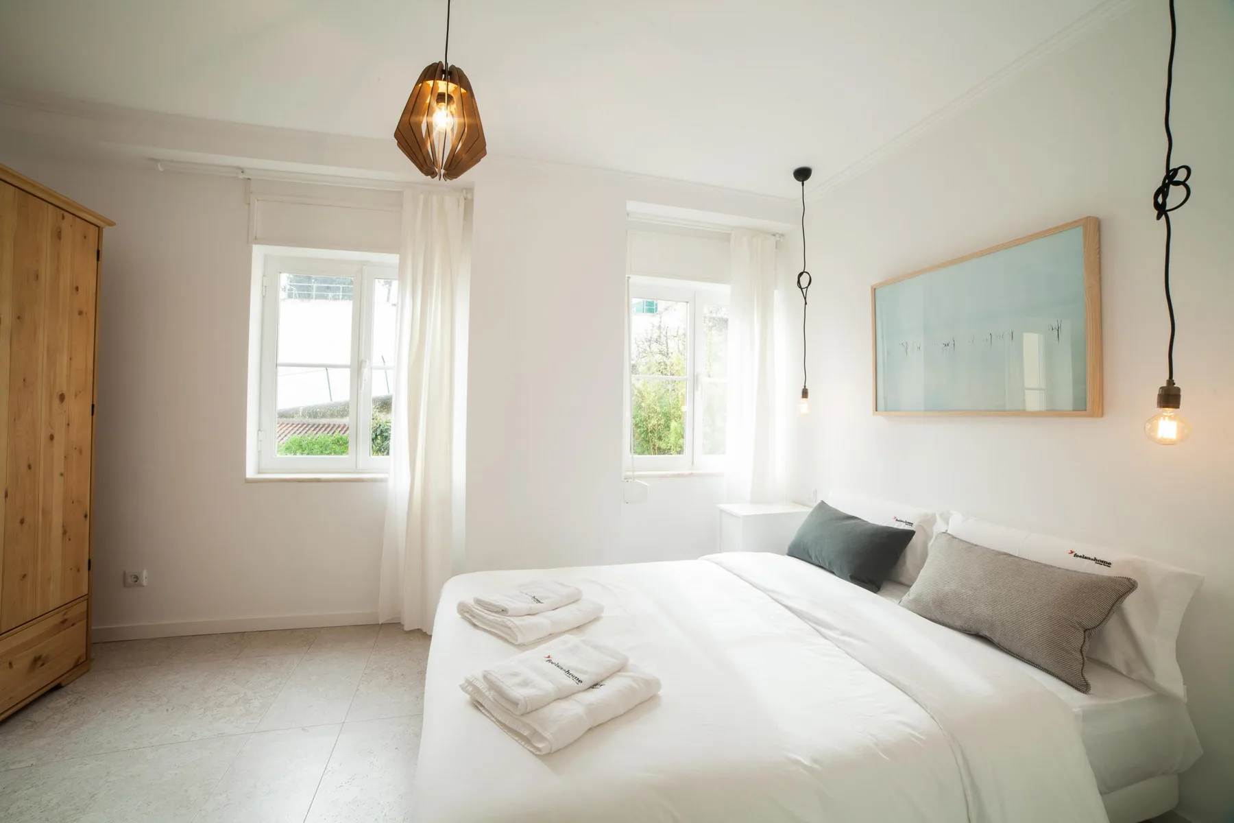 A bright bedroom with a neatly made bed and large windows.