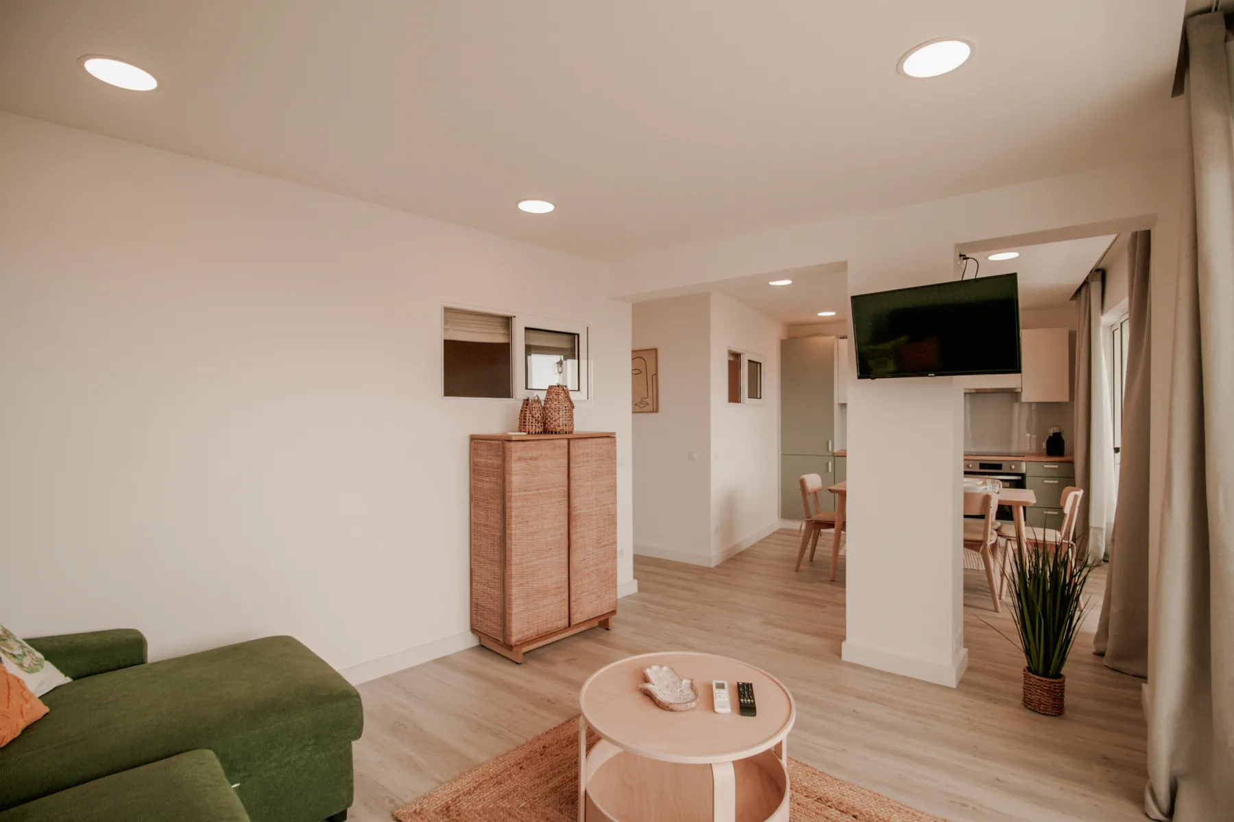 Una sala luminosa con un sofá verde y un comedor al fondo.