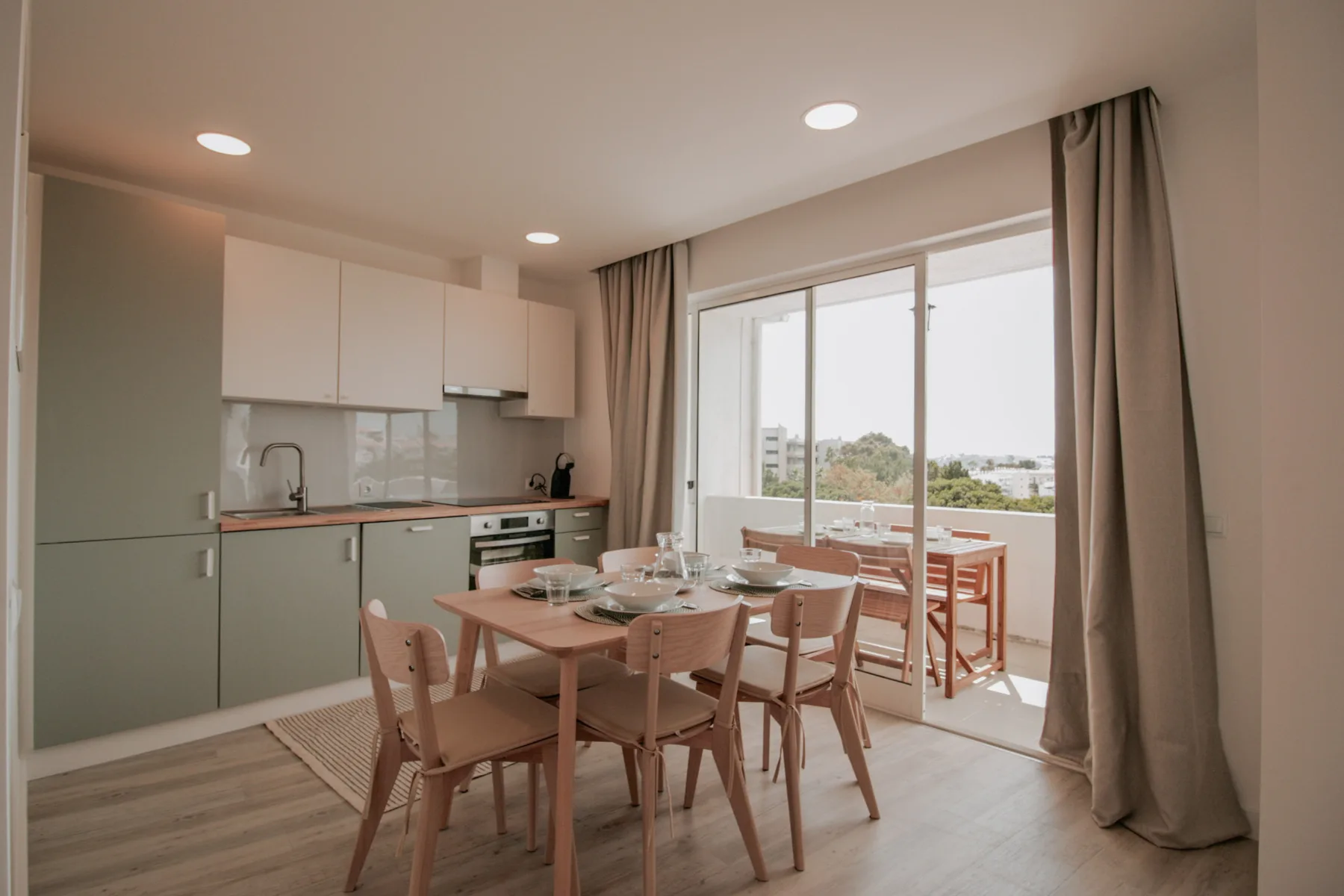 Comedor junto a una cocina compacta y puertas de cristal abiertas a un balcón.