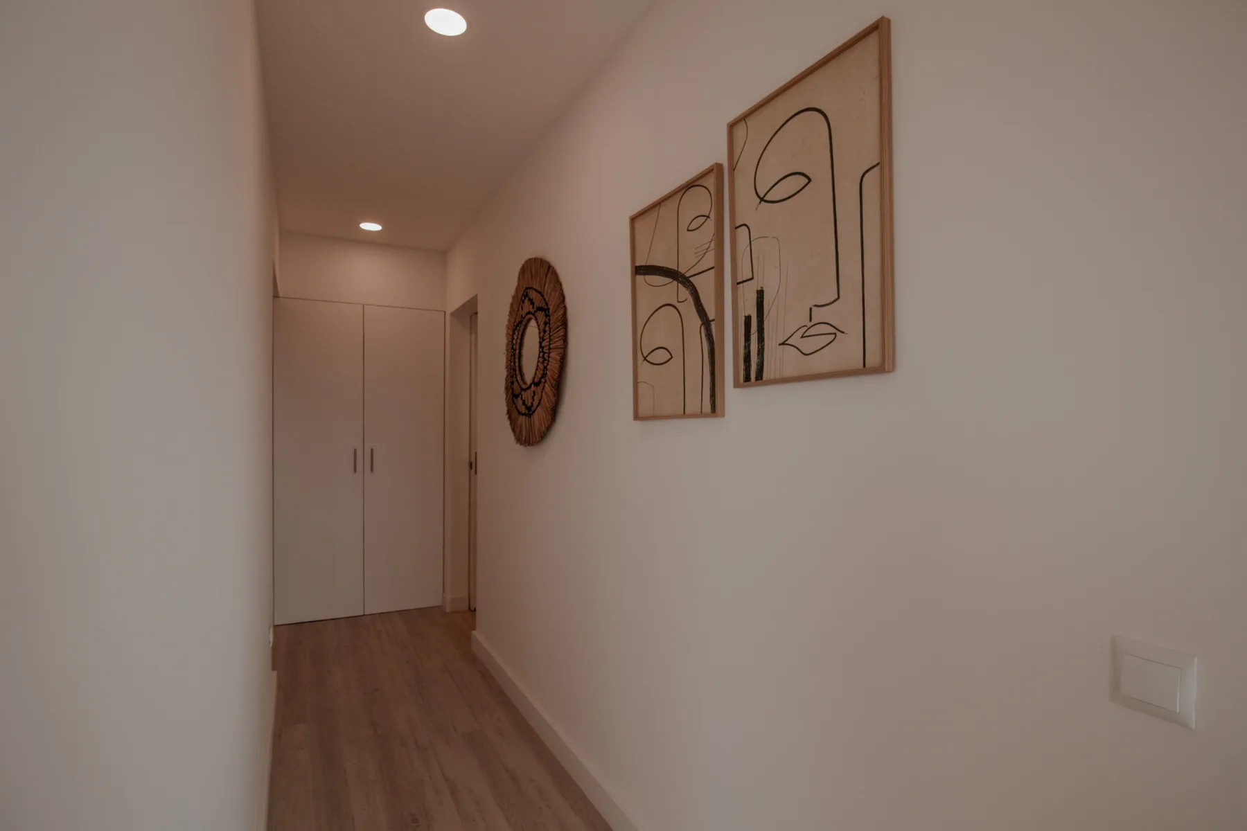 Un pasillo estrecho con suelo de madera y cuadros enmarcados en la pared.