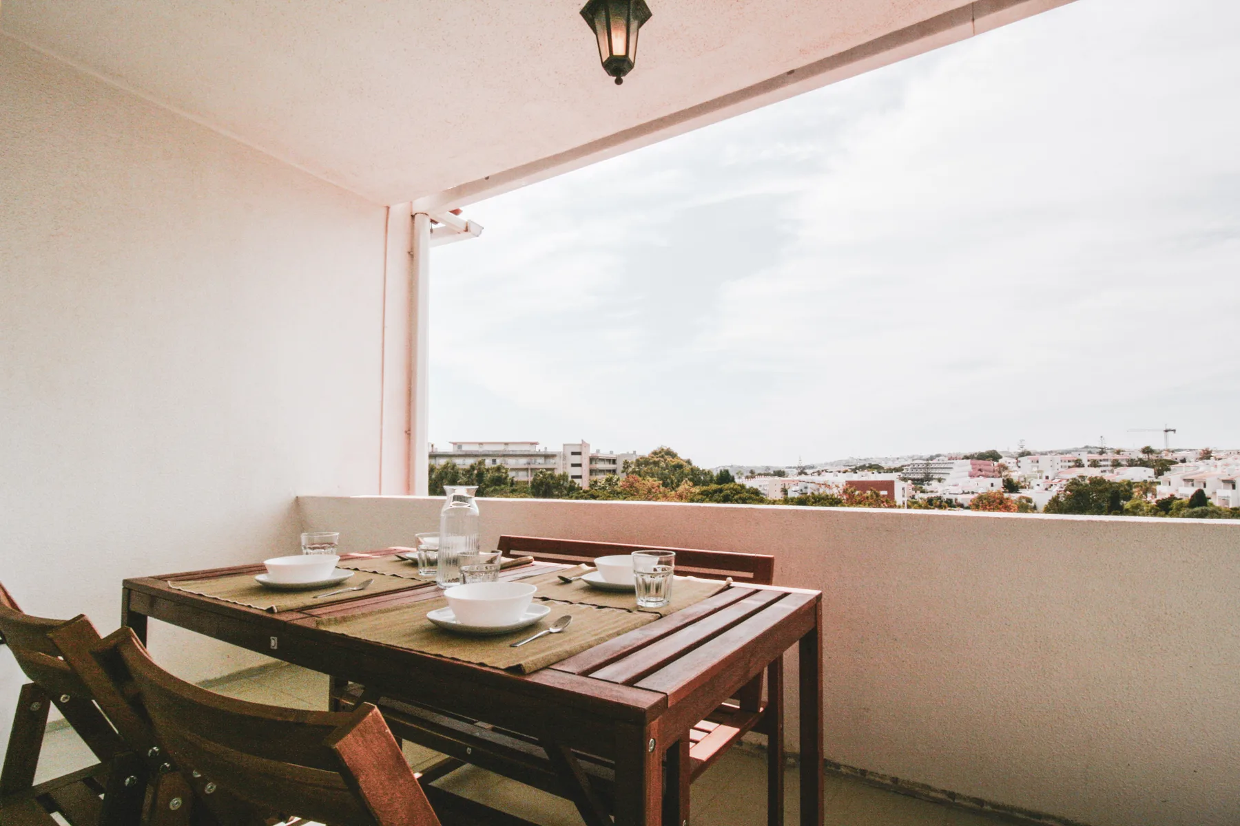 Una zona de comedor en un balcón cubierto da a edificios y árboles cercanos.