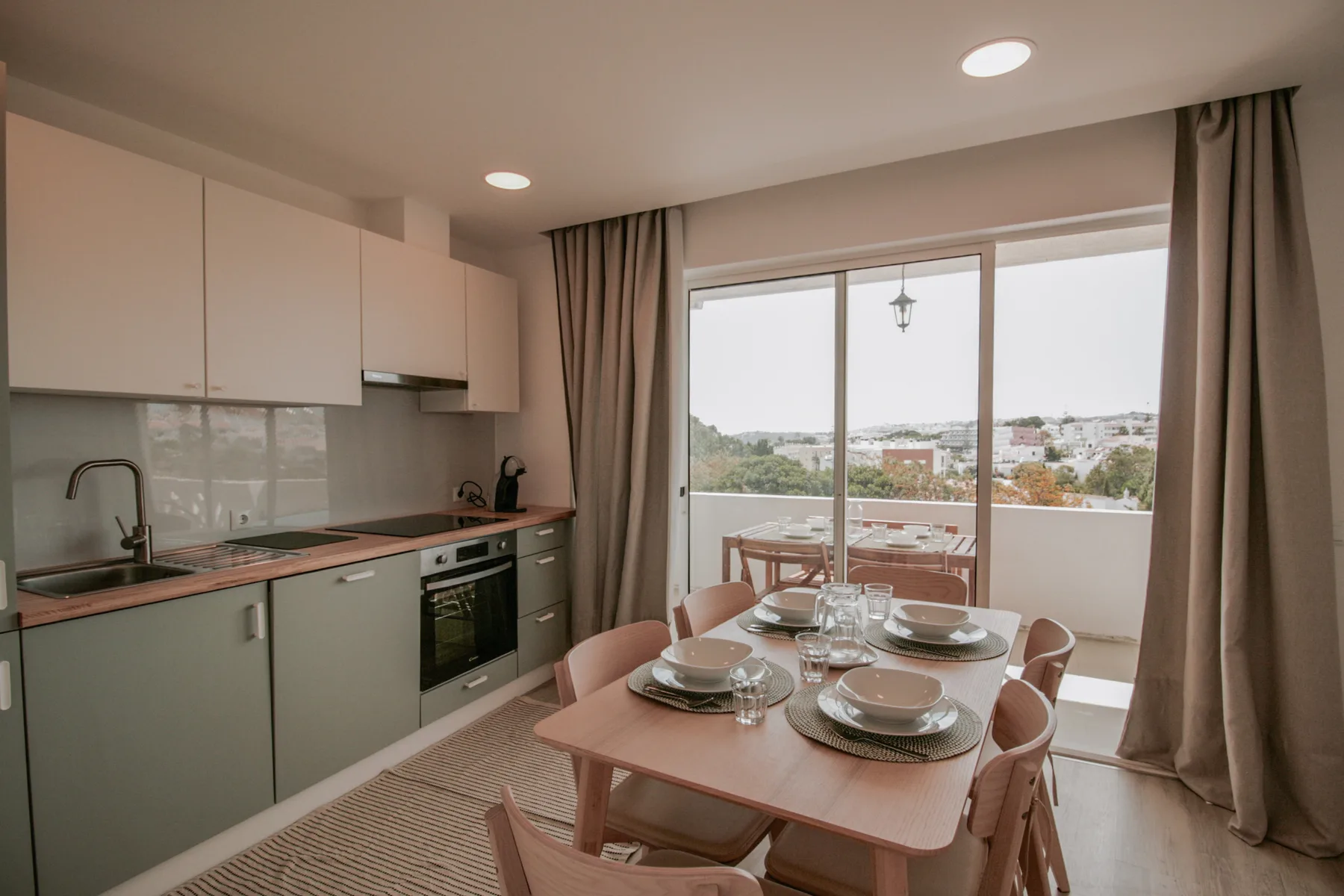 Comedor junto a una cocina compacta, con una mesa preparada cerca de puertas corredizas de vidrio.