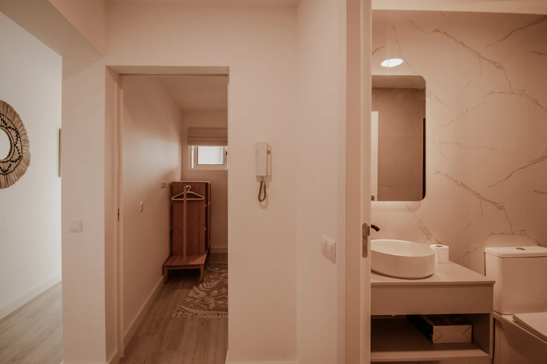 Un pasillo da a un lavabo con lavamanos sobre encimera y espejo.