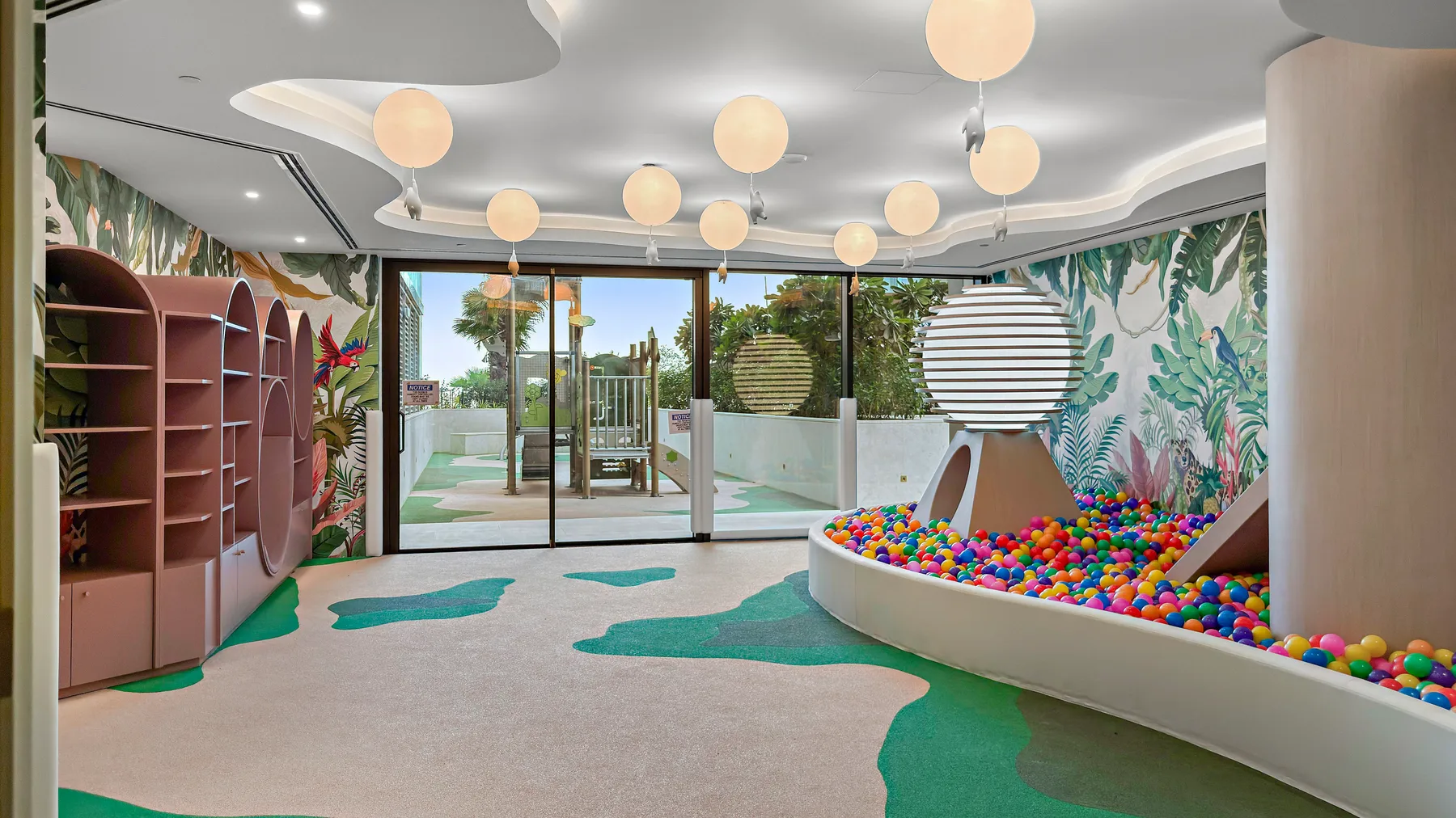 Una colorida sala de juegos interior con piscina de bolas, mural y puertas de vidrio.