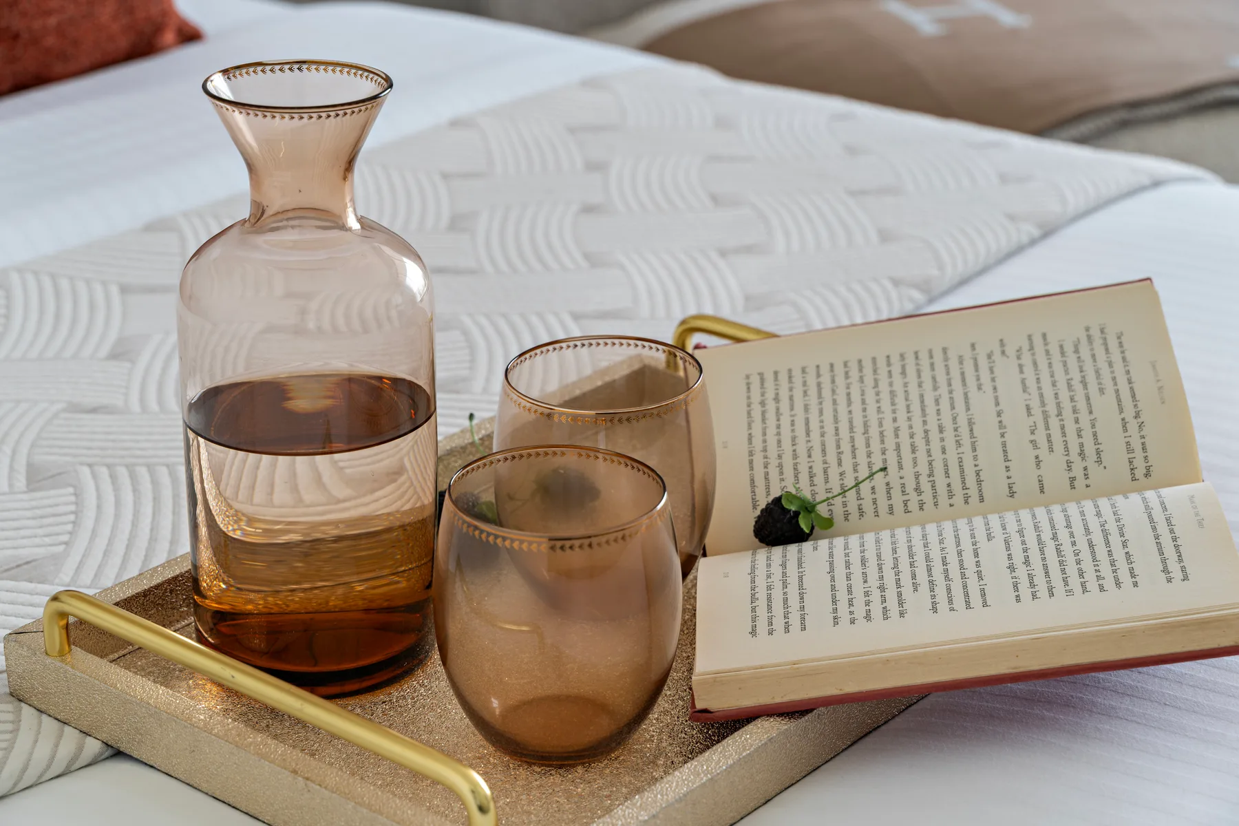 Una cama con una bandeja que sostiene vasos y un libro abierto.