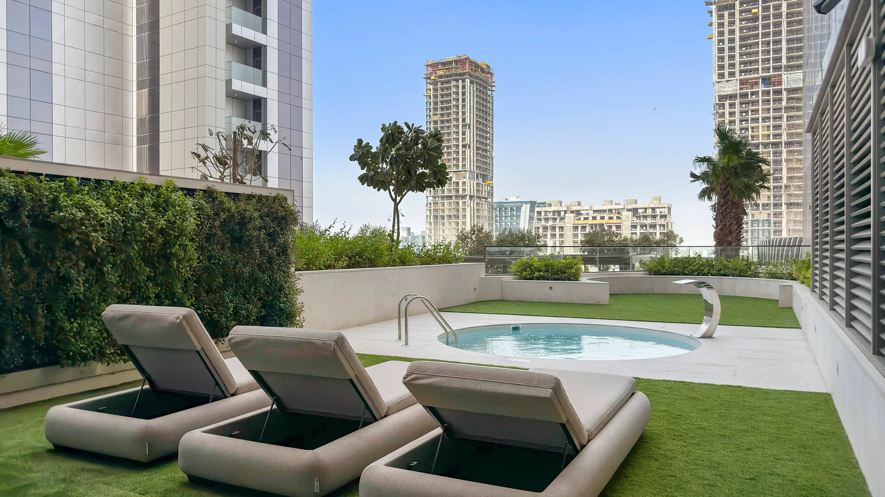 Zona de piscina al aire libre con asientos reclinables y edificios altos alrededor.