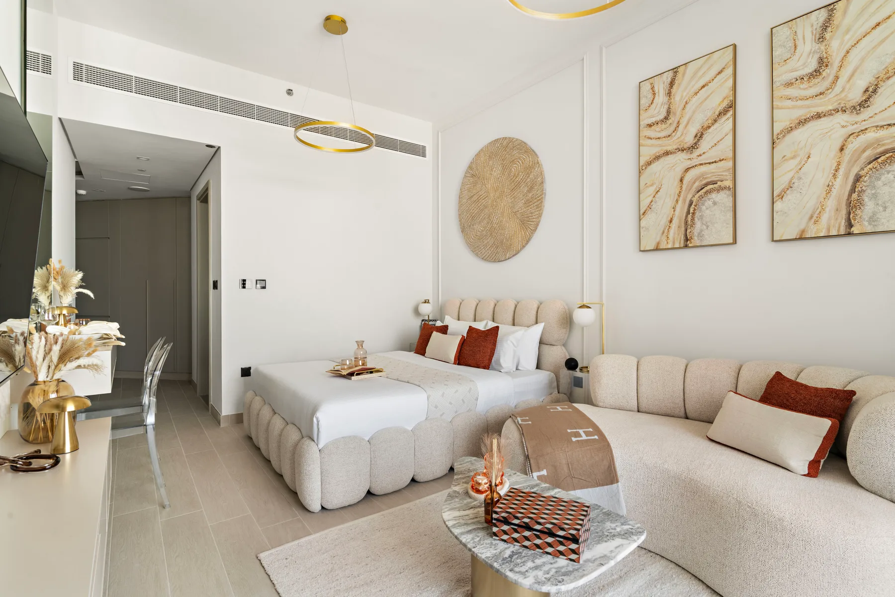 Un dormitorio luminoso con una cama grande, asientos tapizados y arte abstracto en las paredes.