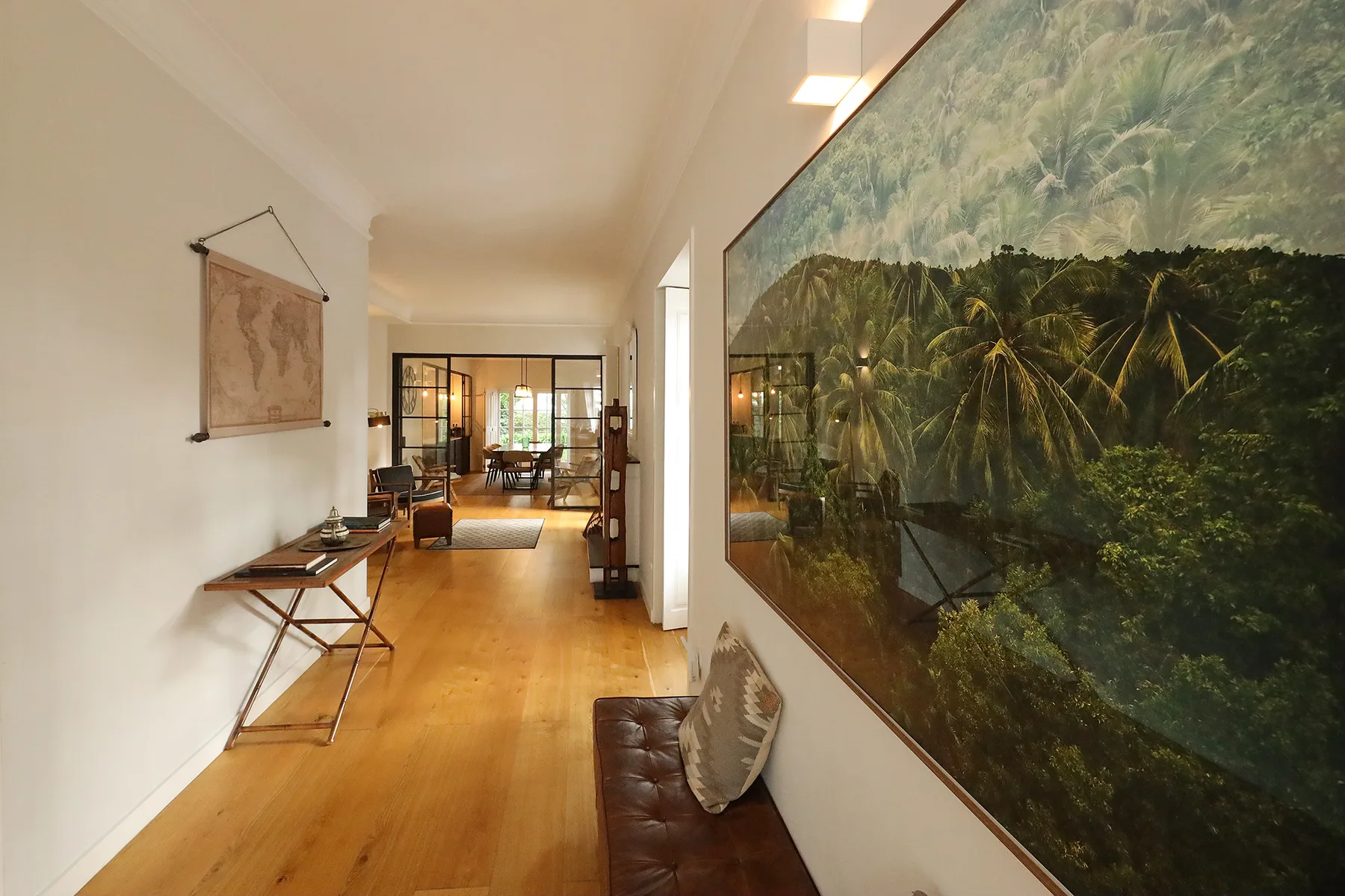 A hallway with wooden flooring and a large tropical landscape painting.