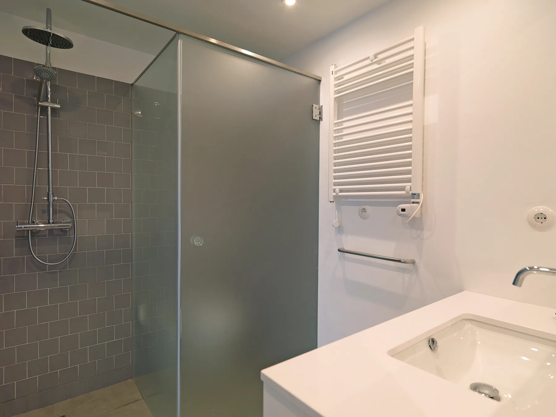 A bathroom with a glass shower, wall-mounted towel warmer, and sink.