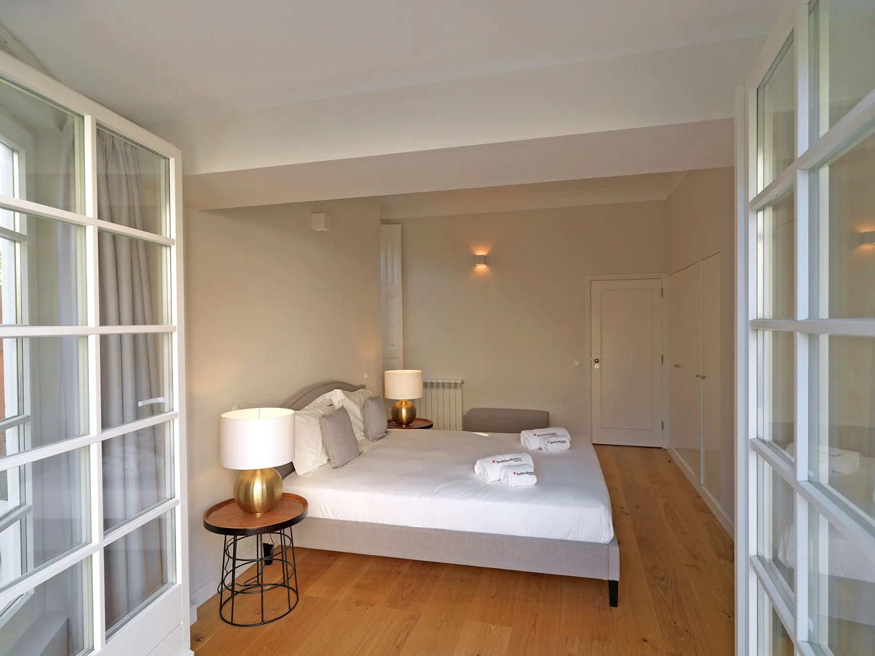 A bright bedroom with a large bed, bedside lamps, and wooden flooring.