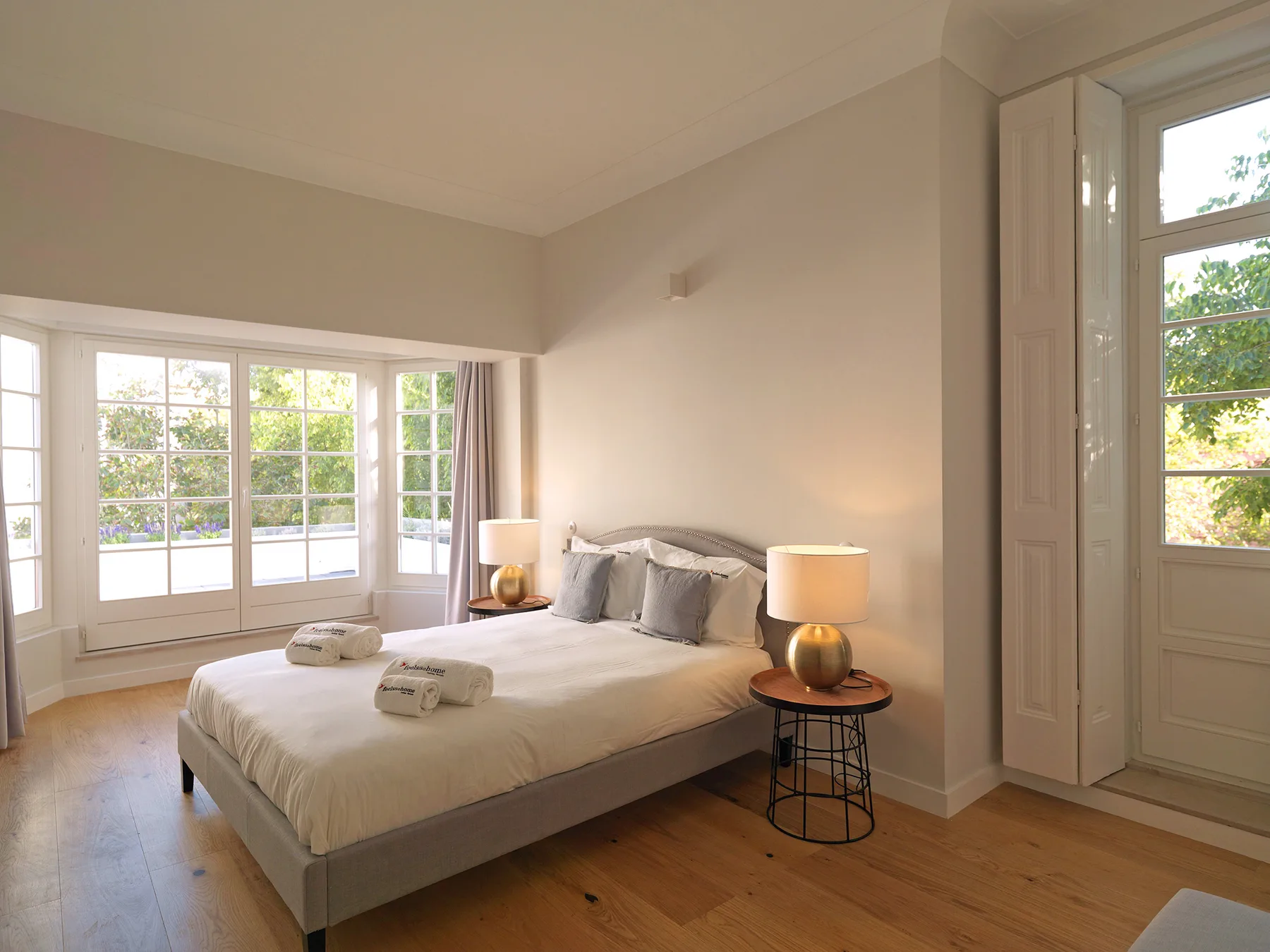A bright bedroom with a bed, bedside table, and large windows.