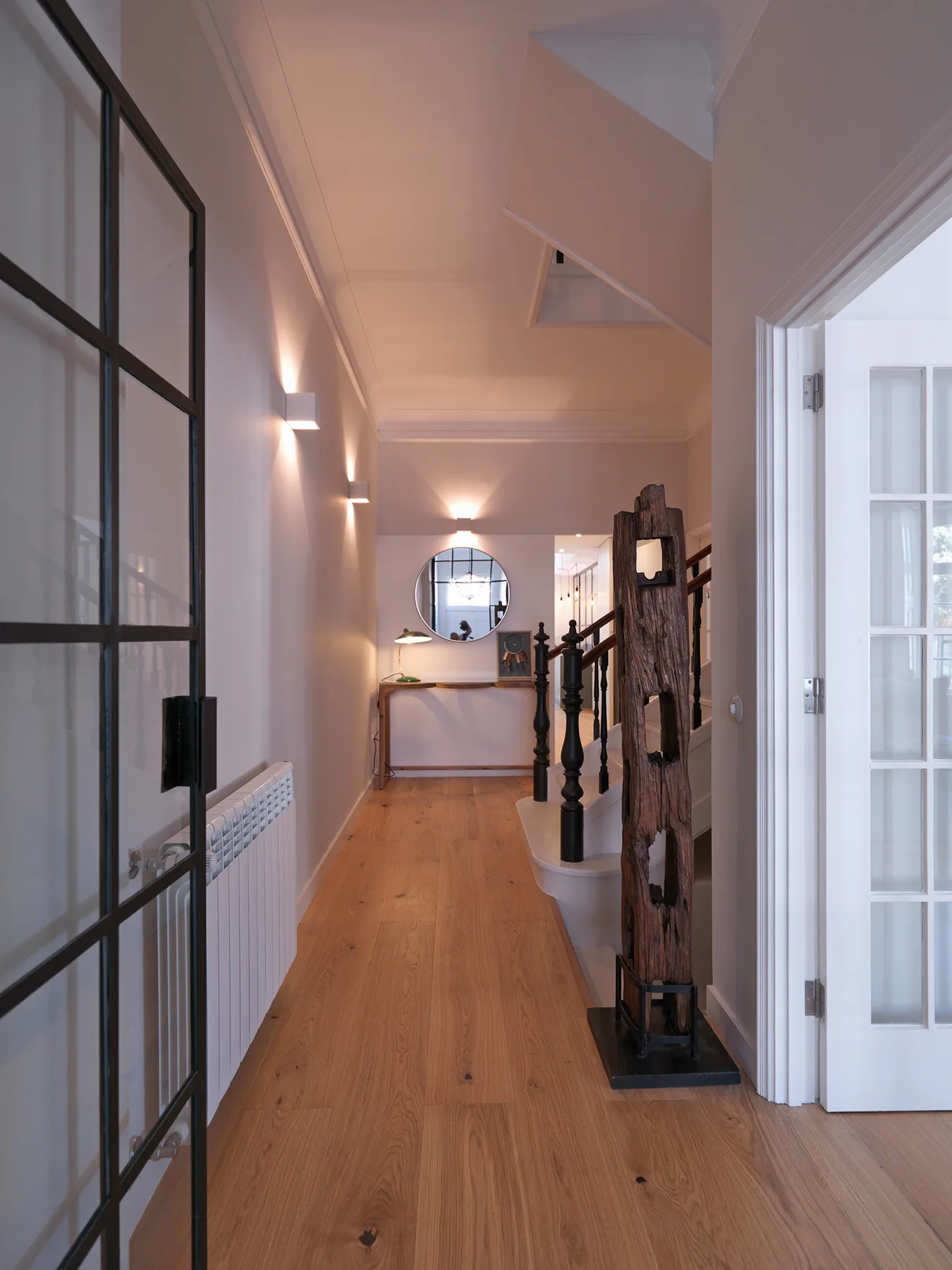 A hallway with wood flooring, wall lights, and a console at the far end.