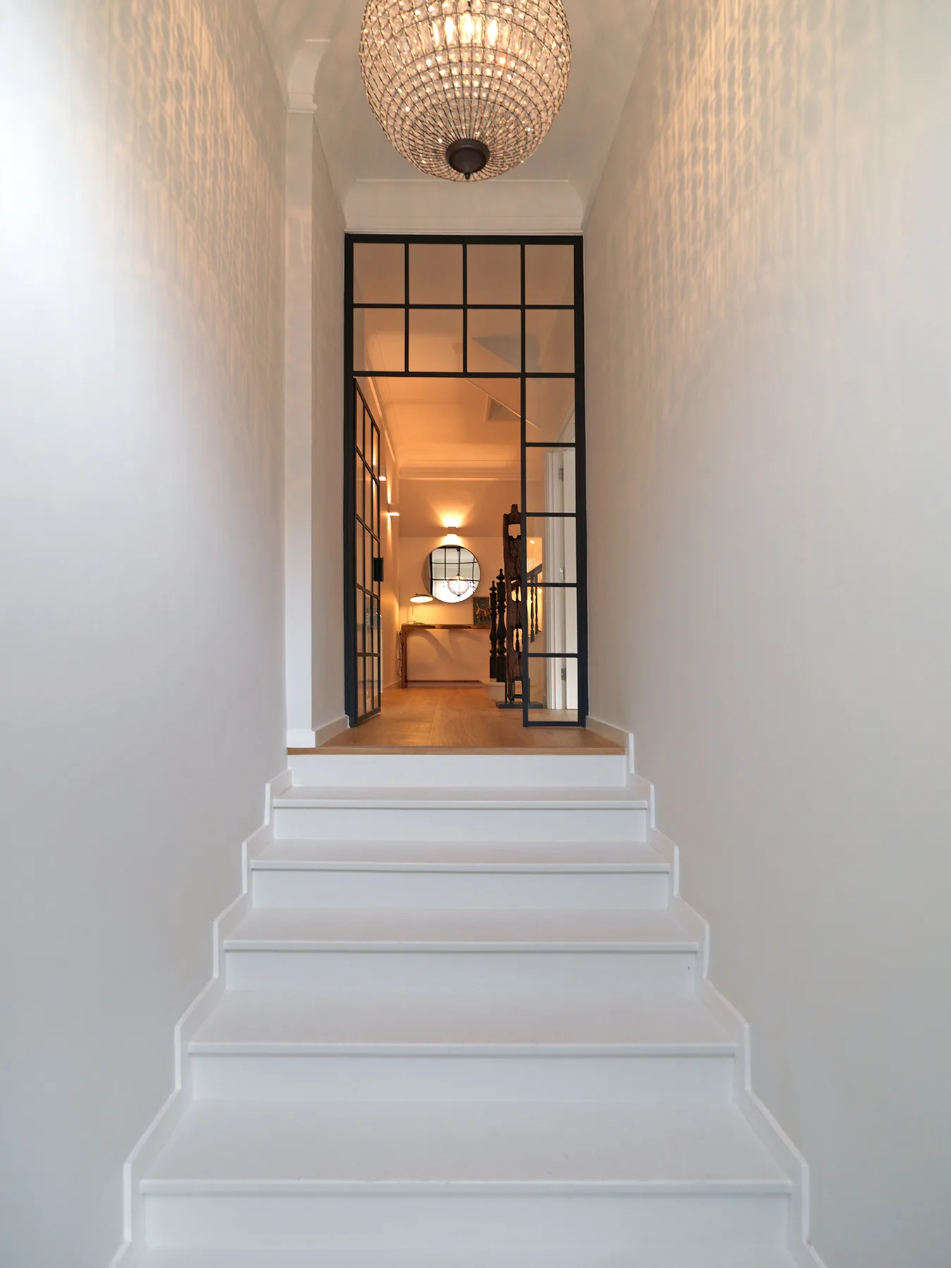 A bright interior staircase leads to a black-framed glass partition and warmly lit room.