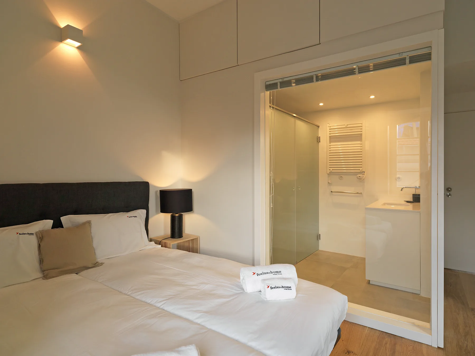 A bedroom with a neatly made bed and an open view into the bathroom.