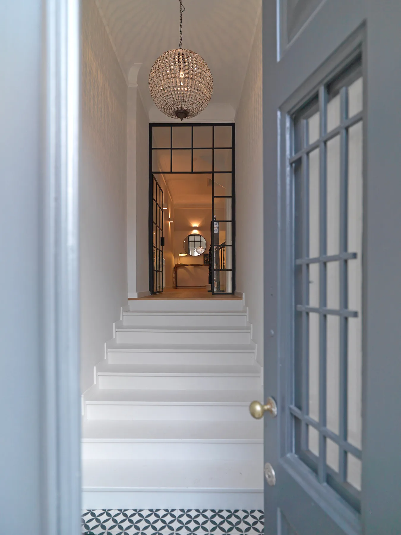 A white staircase leads through a glass-paneled doorway into a warmly lit interior.